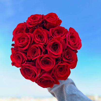 Ramo de rosas rojas con el cielo de fondo sostenido por una persona en chaqueta de blue jean